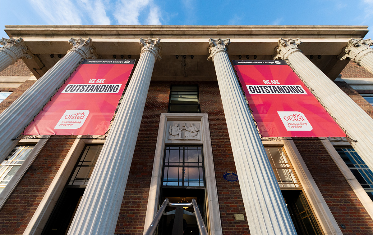 Looking up the pillars of the College towards a blue sky. Two banners sit between the pillars.